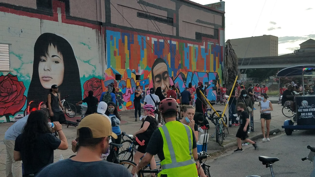 Juneteenth cyclists stop the ride to gather at the George Floyd mural in EaDo, next to a mural of Selena Quintanilla.