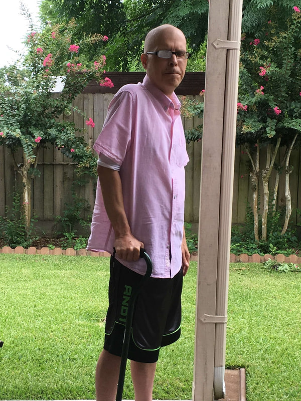 Photo of blogger Harry Hamid in a back yard, wearing a pink guayabera shirt and clutching his walking cane.